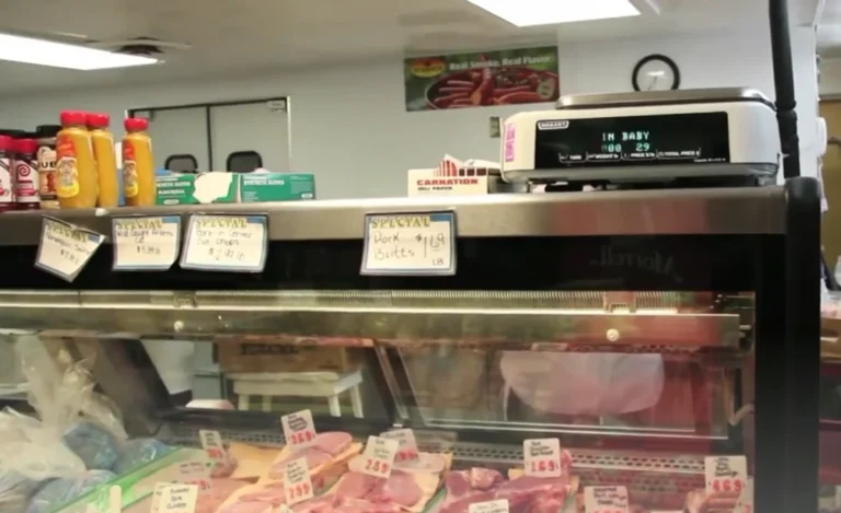 Mosier's Meat Market counter, Raymond OH, handing fresh-cut steaks to customer beside glass case of smoked sausages